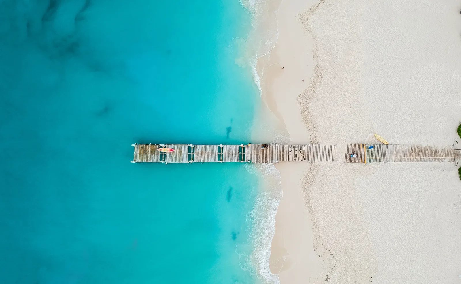 A wooden pier reaching over the turquoise shallows of Grace Bay